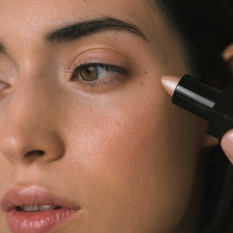 Perfil de mujer aplicando iluminador color rosa intenso